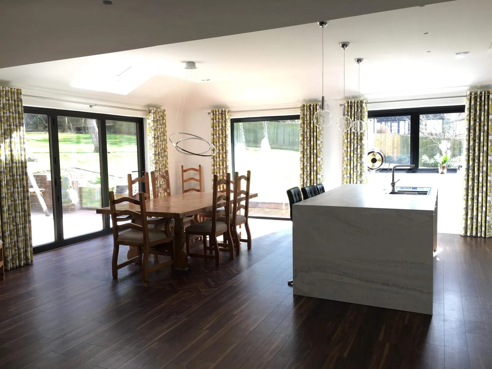Patterned curtains at three sets of garden doors in an open-plan kitchen and dining room
