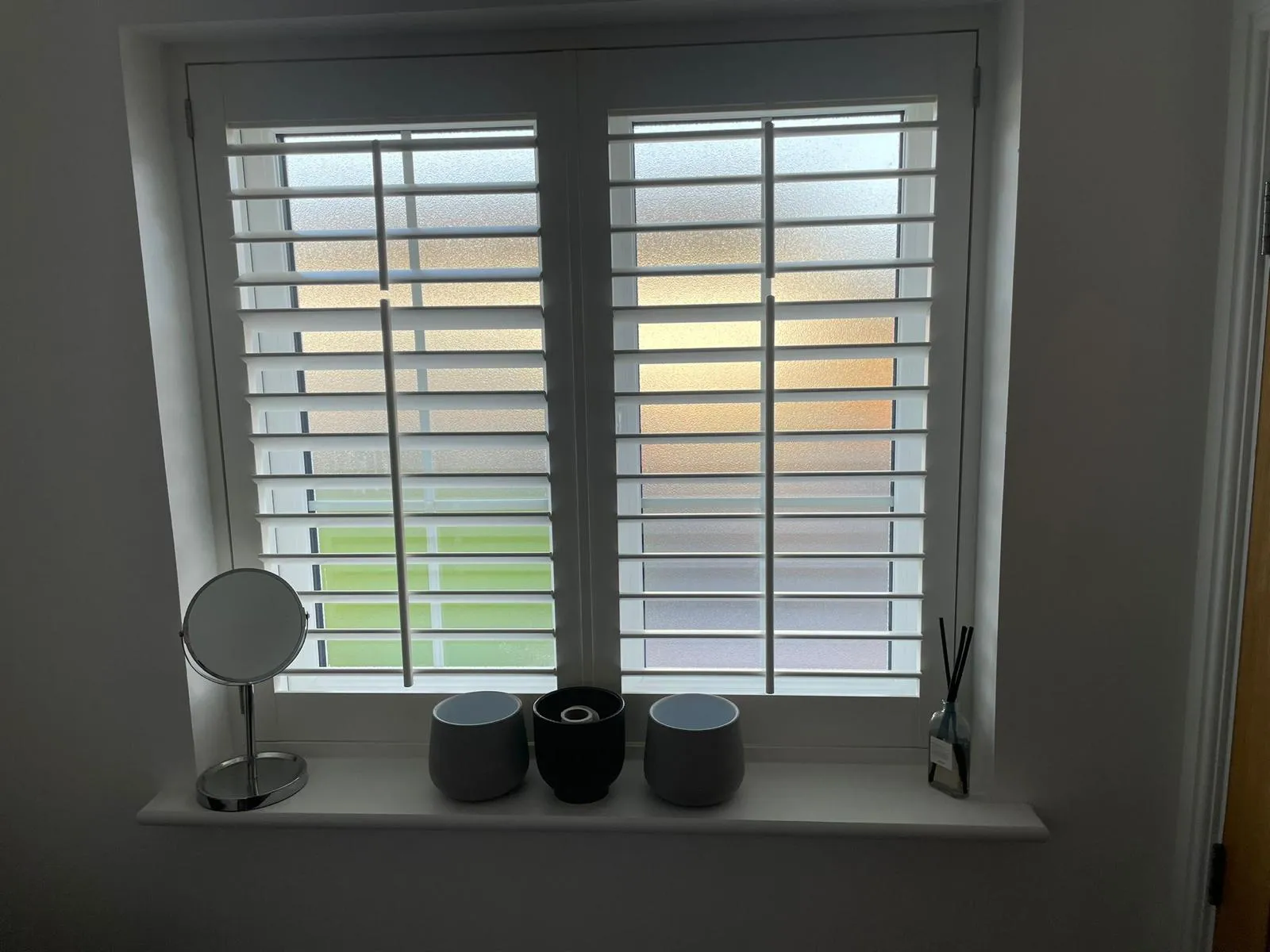 White plantation shutters with open louvres on a frosted bathroom window