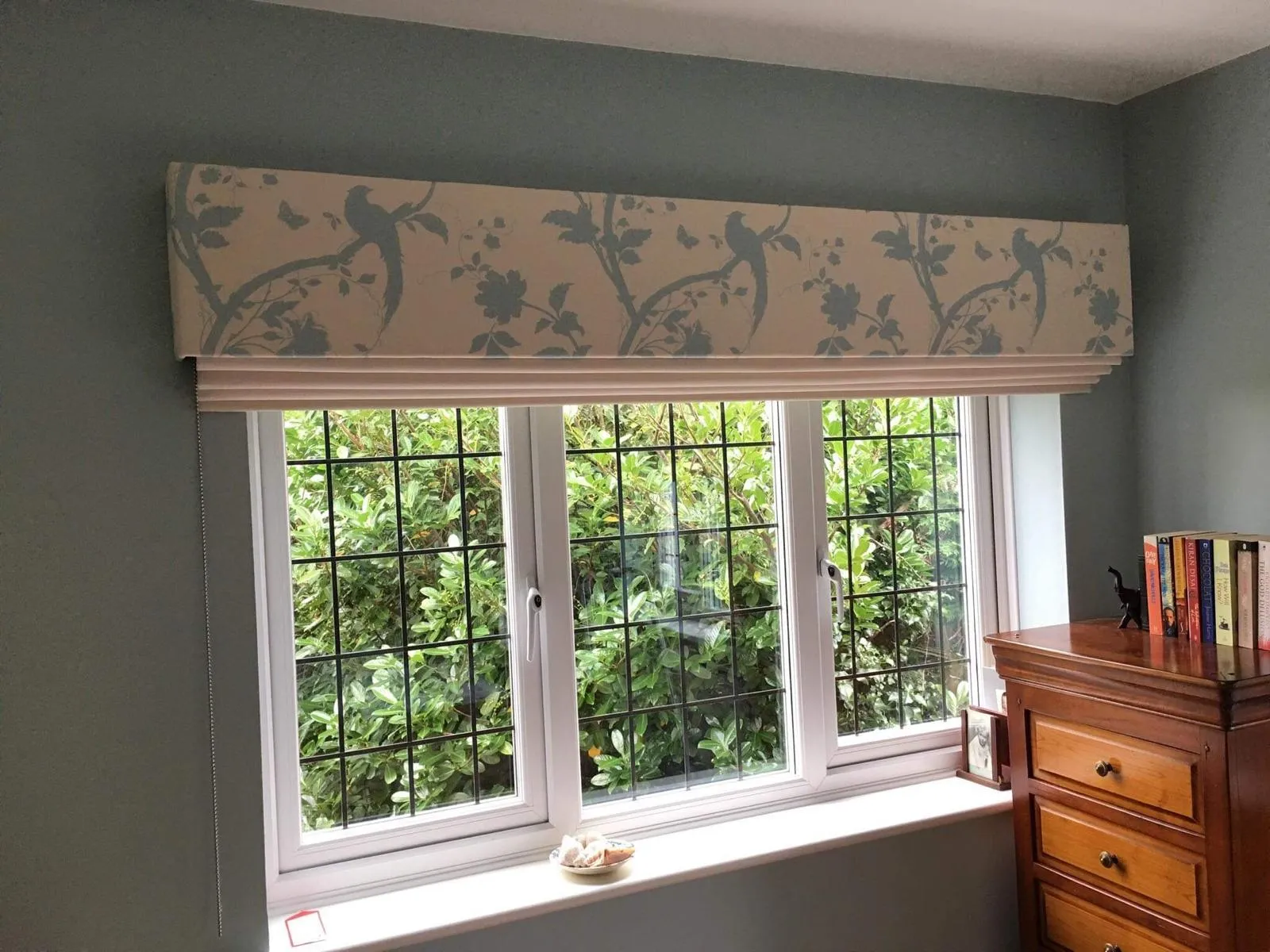 Upholstered bird-print pelmet above a leaded casement window in a green-painted room