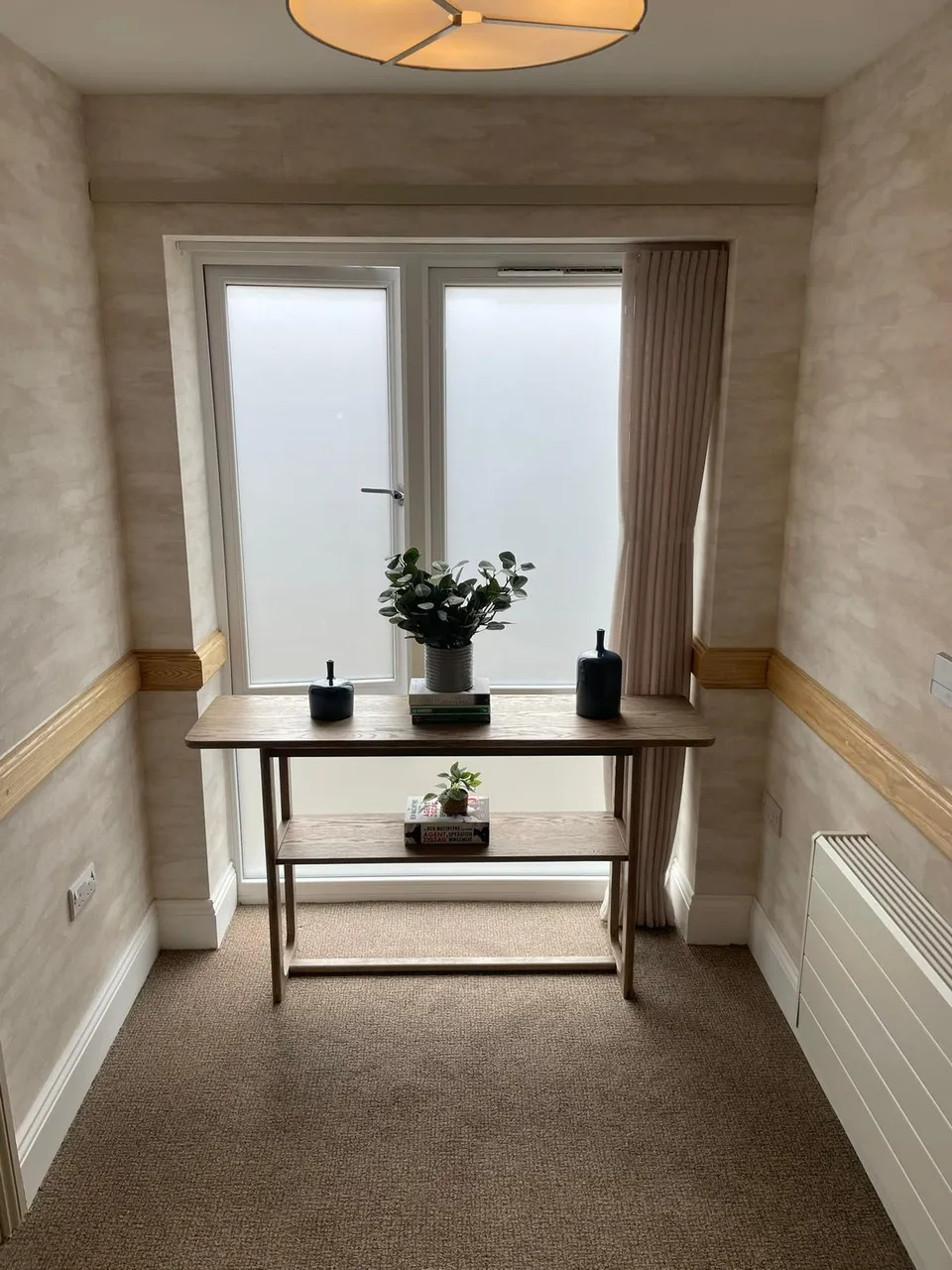 Cream curtain panel beside a frosted window on a landing with a console table and plant