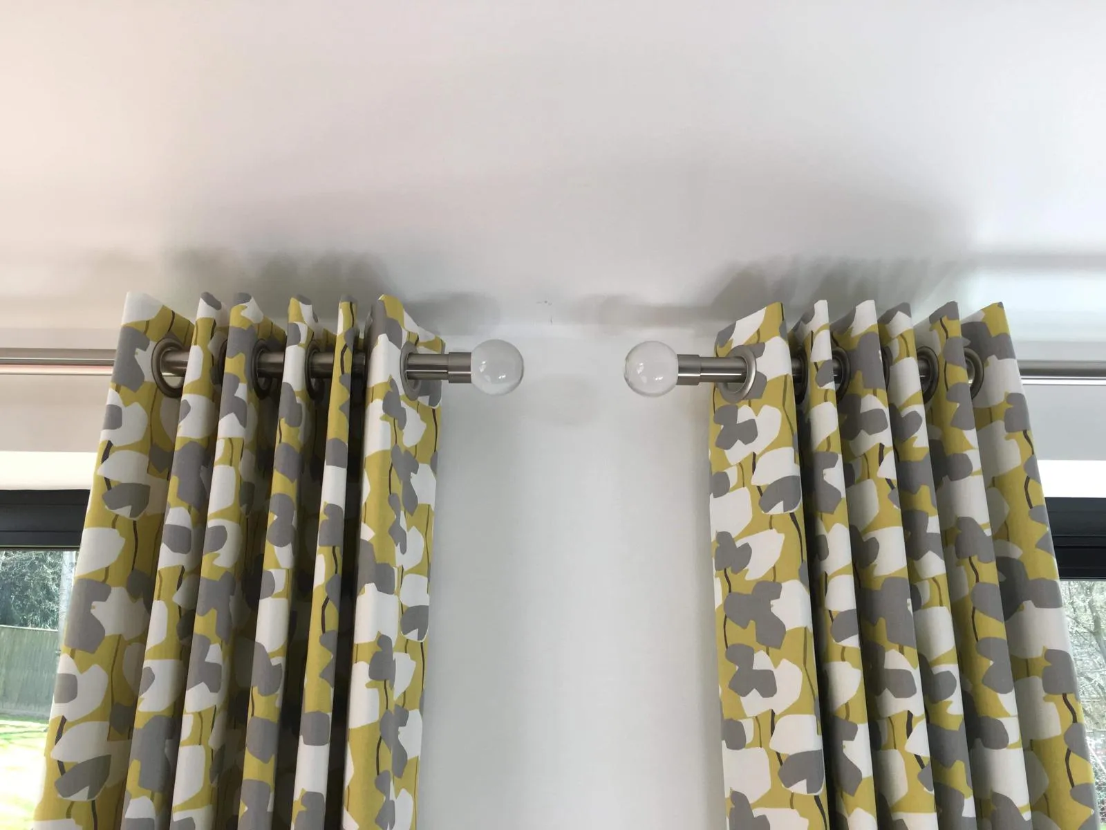 Two metal curtain poles with rings and brackets carrying patterned pinch-pleat curtains