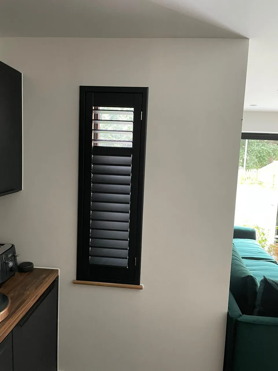 Black plantation shutters on a tall narrow window in an open-plan kitchen and living area
