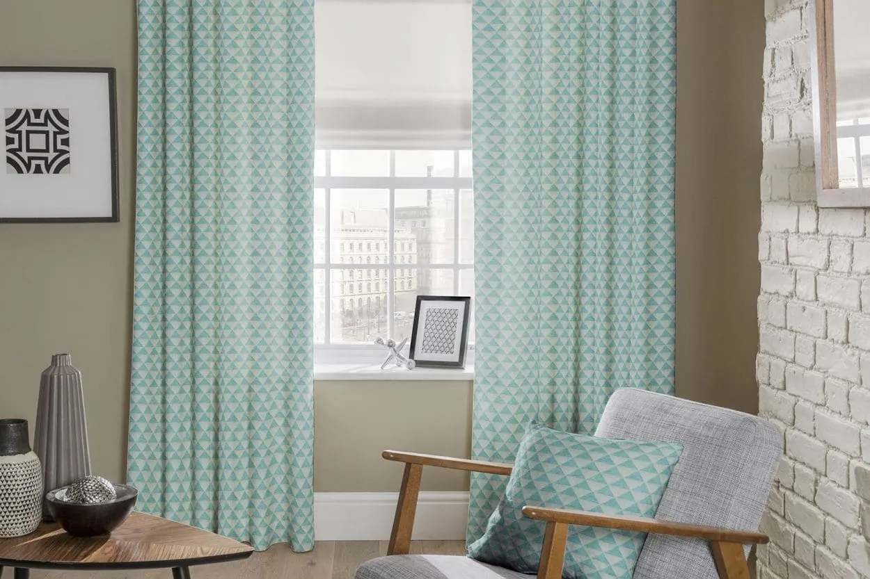 Aqua triangle print curtains framing a sash window with a white Roman blind and a matching cushion