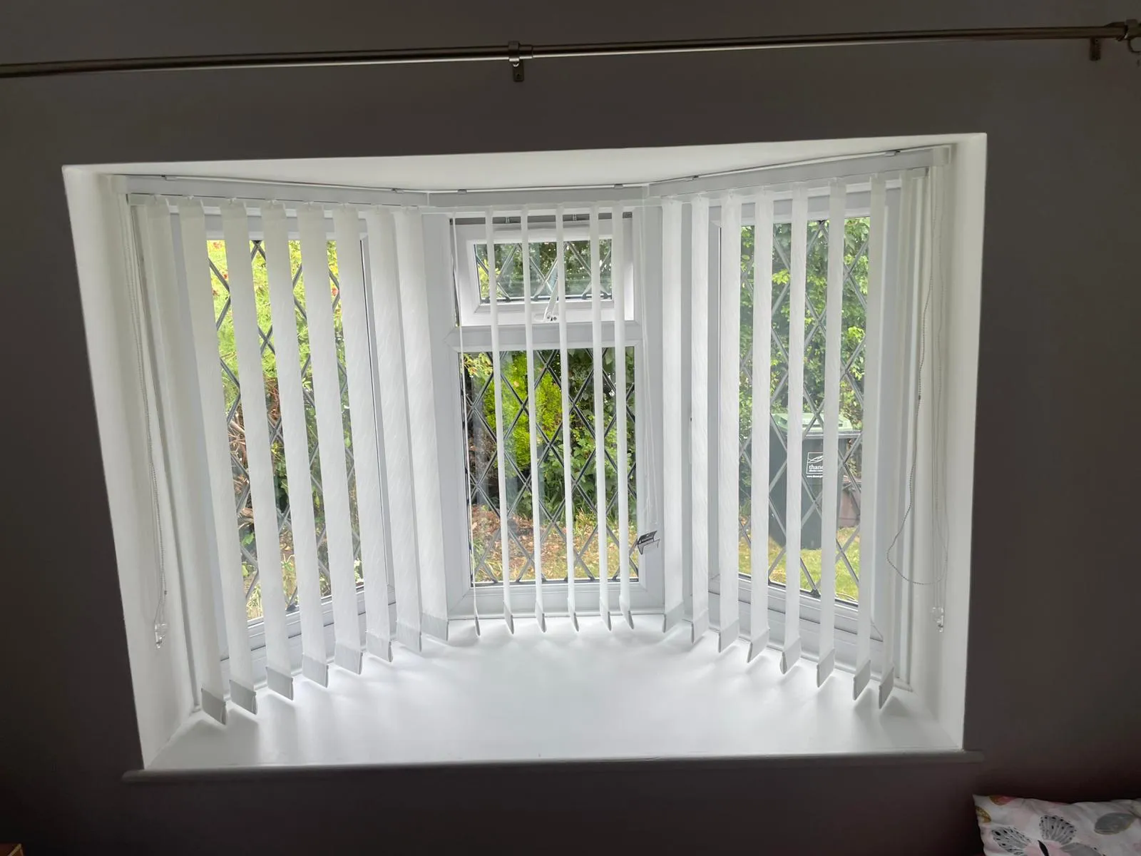 White vertical blinds in a square bay window with leaded panes and a garden view