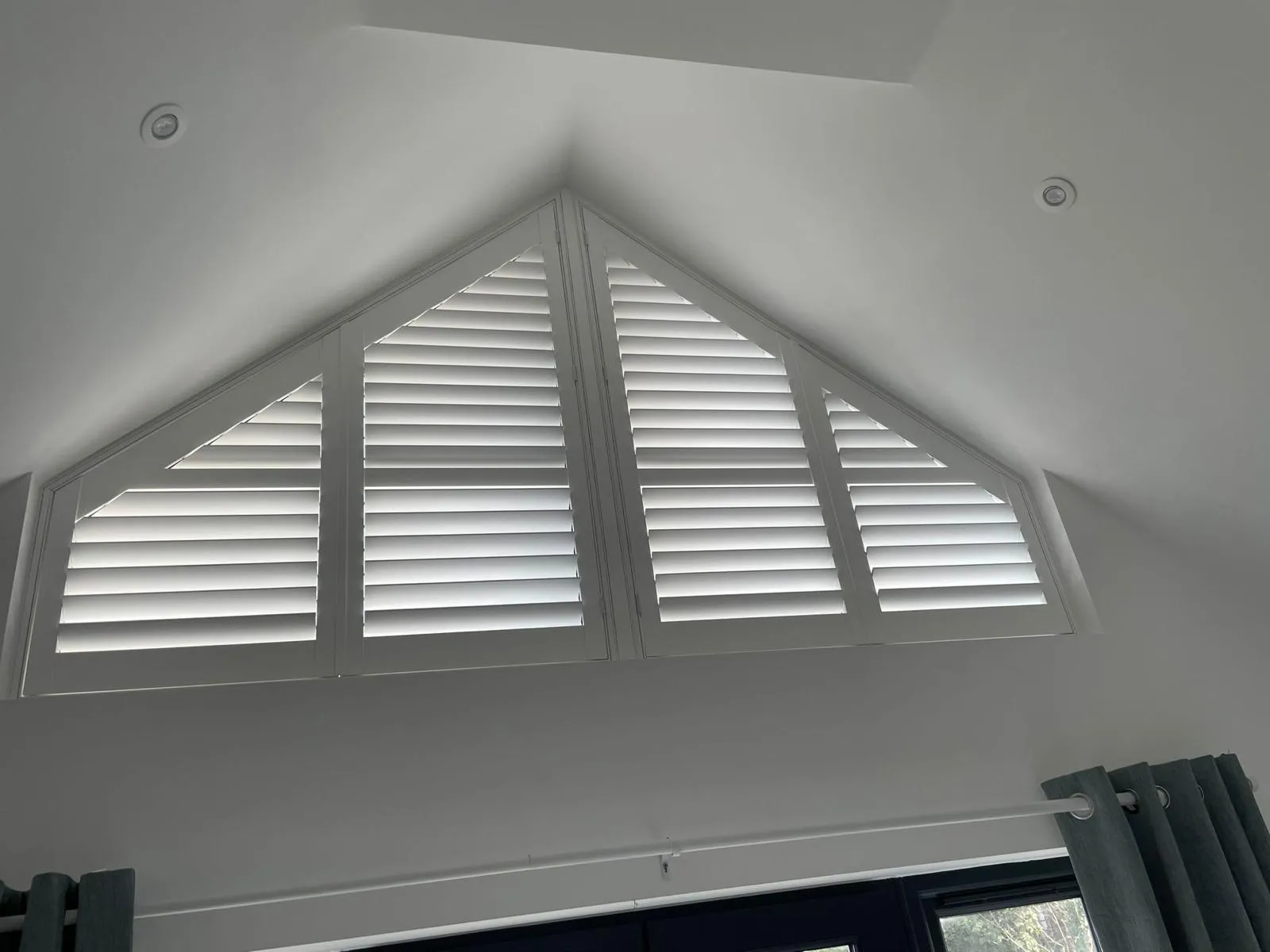 Shaped white plantation shutters in a triangular gable window under a vaulted ceiling