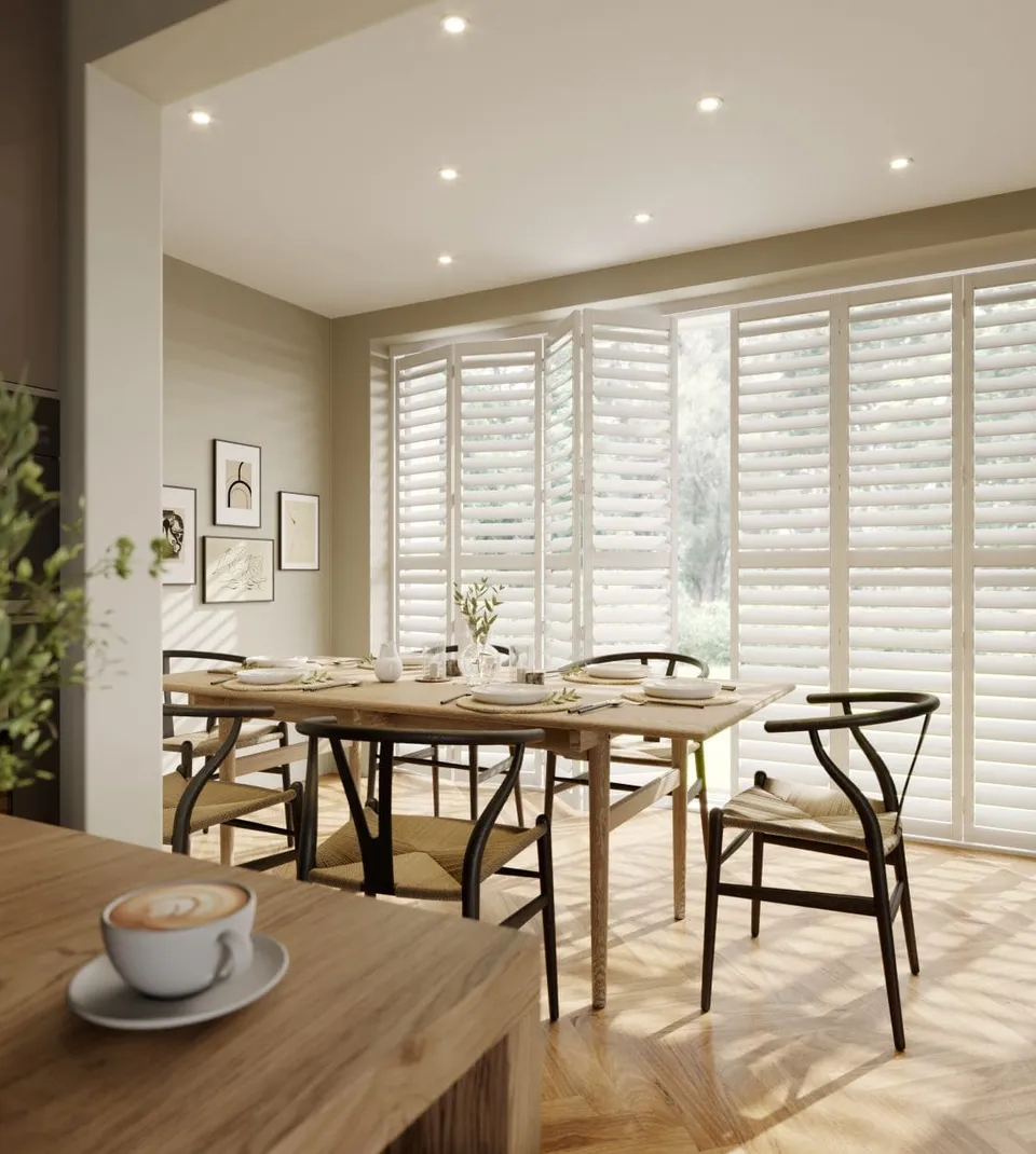 White tracked shutters folded back from a garden door behind a set dining table